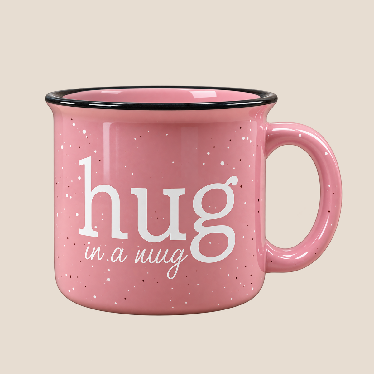 A pink speckled enamel mug with a black rim and handle, featuring the white text 'hug in a hug' on the front, set against a solid beige background.