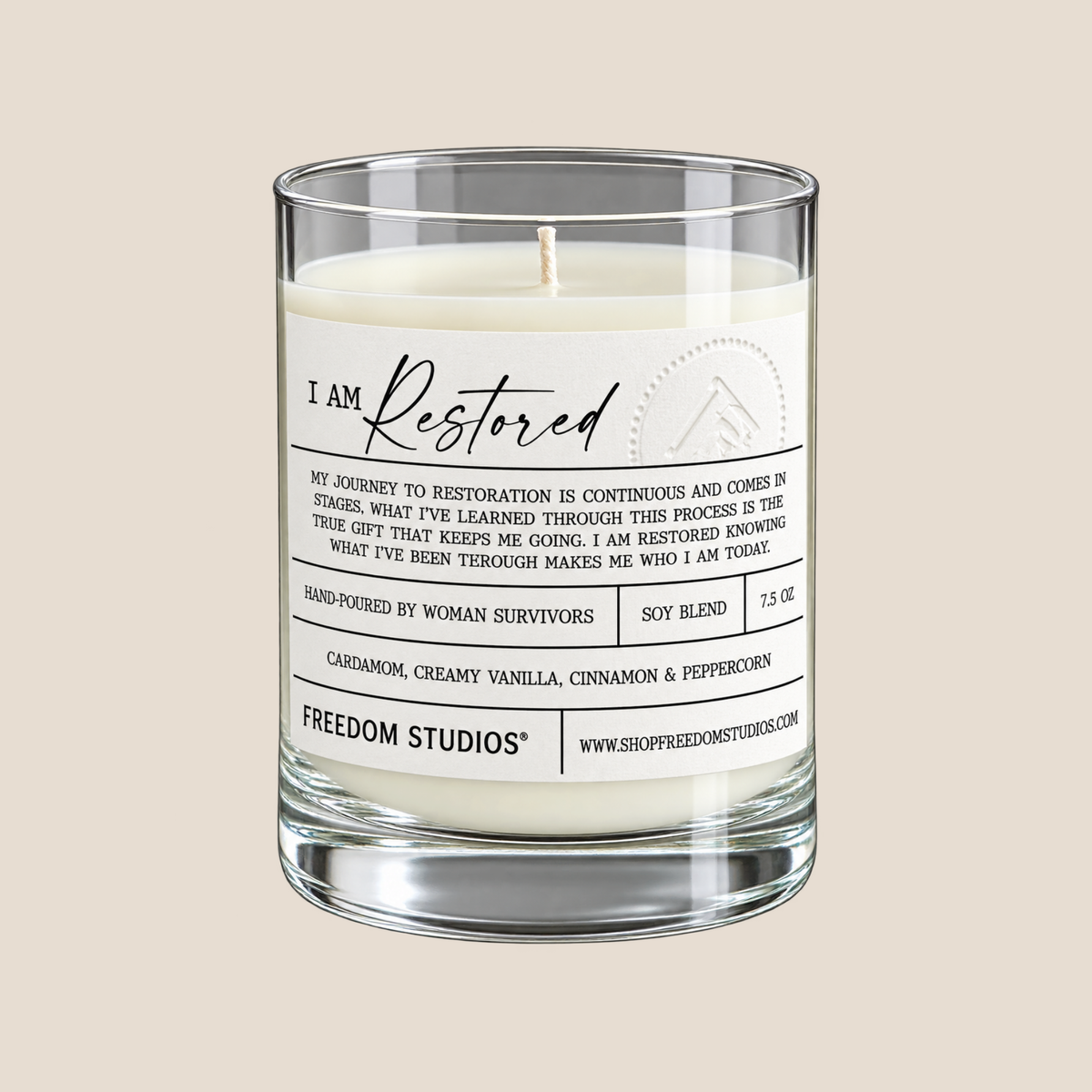 A clear glass jar candle with white wax and a printed white label reading 'I Am Restored' and 'FREEDOM STUDIOS' on a light beige background.