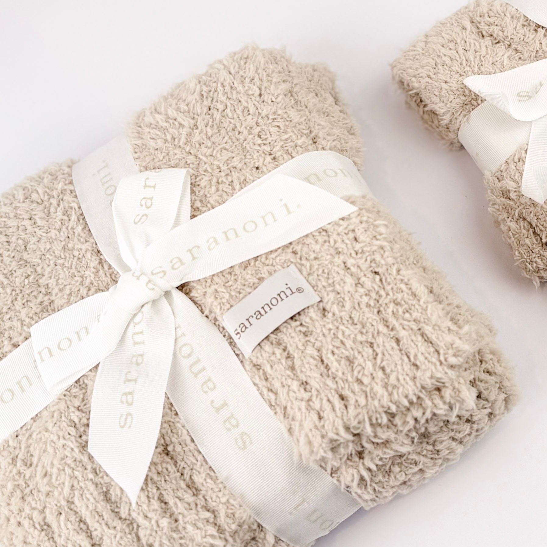 Beige blanket with a white ribbon and 'Saranoni' label on a light background