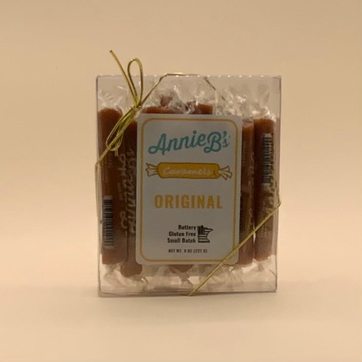 Annie B's Caramel Bars in a clear plastic clamshell package tied with a gold string, on a beige background.