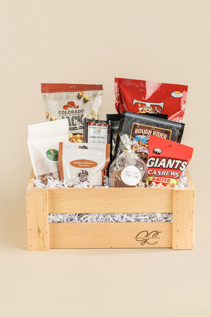 Gift basket with snacks and treats in a wooden crate on a beige background