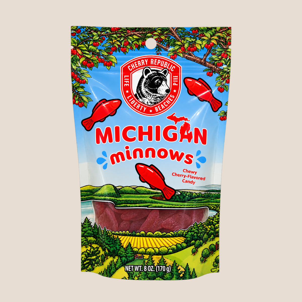 A stand-up pouch of Cherry Republic Michigan Minnows chew cherry-flavored candy, featuring a colorful illustration of a cherry orchard, river, and landscape with red fish graphics on a light beige background.