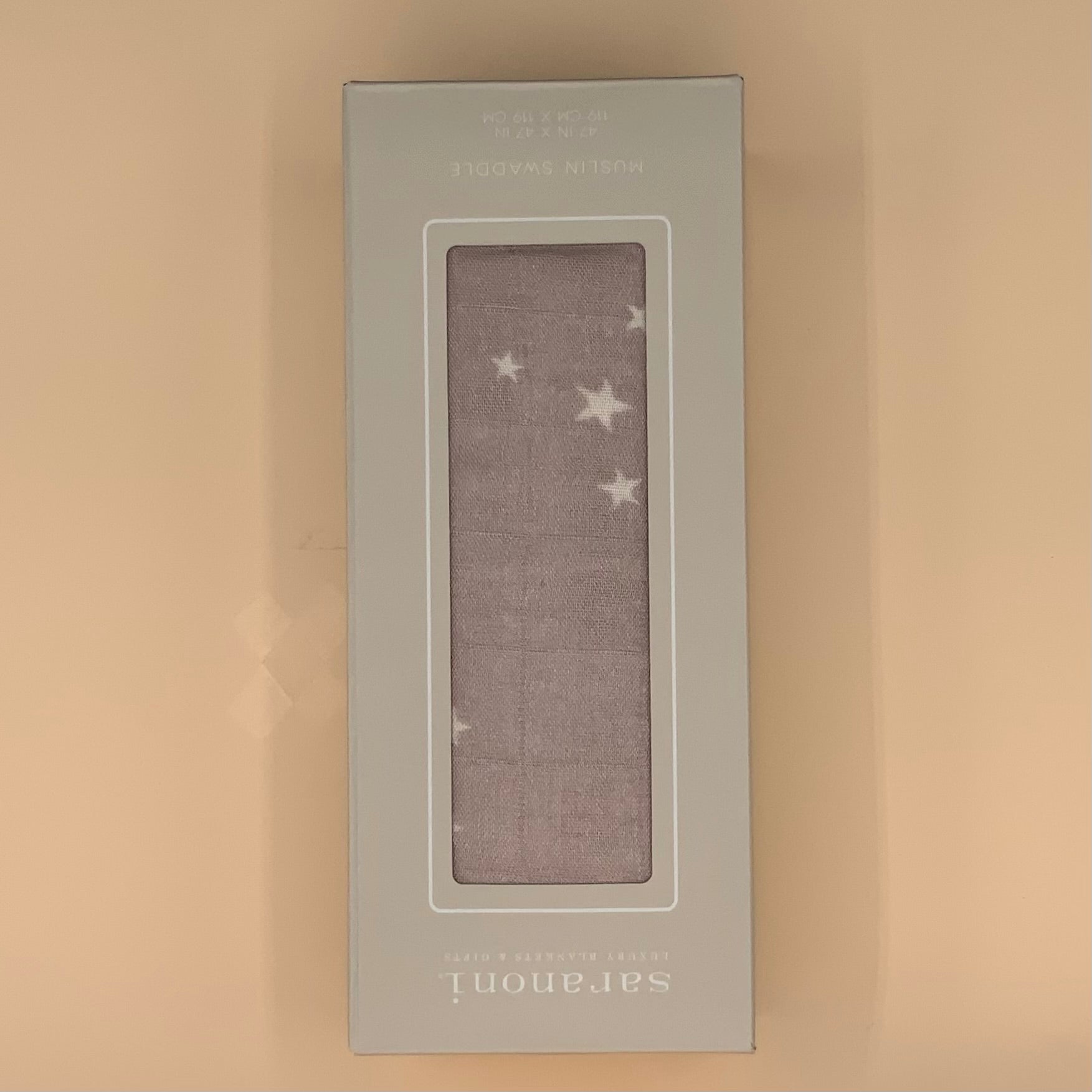 A packaged baby blanket or swaddle shown in its box, with a rectangular clear window revealing a soft gray blanket printed with white stars. The box is light gray and stands against a plain beige background.