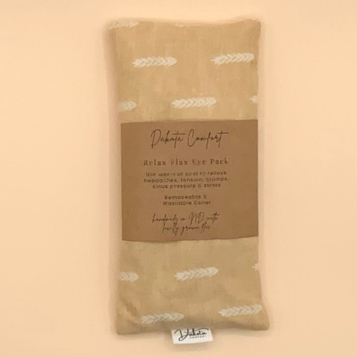 A beige fabric Relax Plax Eye Pack with a brown paper label, featuring a white feather pattern, set against a solid beige background.